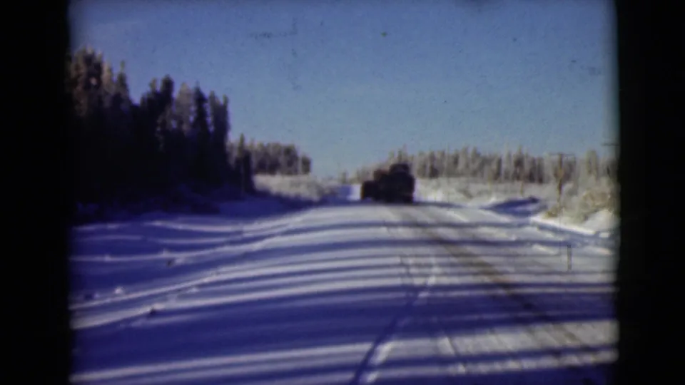 1946 Alaska 8mm frame showing a distant vehicle on a snow-packed wooded road with visible tire marks.