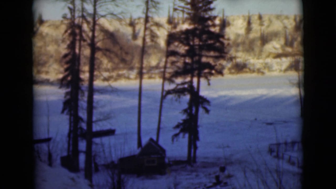 1946 Alaska 8mm frame showing a snow-covered Peace River landscape with trees, pale hills, and a small cabin-like structure.