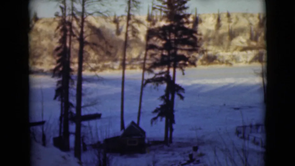1946 Alaska 8mm frame showing a snow-covered Peace River landscape with trees, pale hills, and a small cabin-like structure.