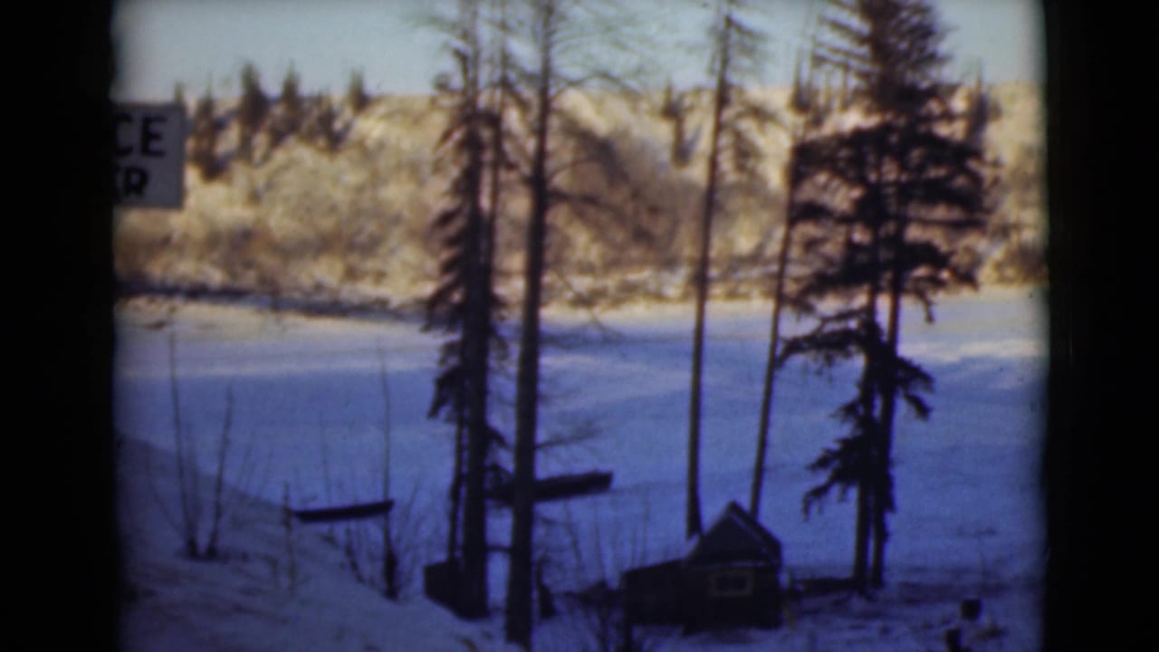 Snowy river scene with tall trees and a partly visible sign at the left edge.