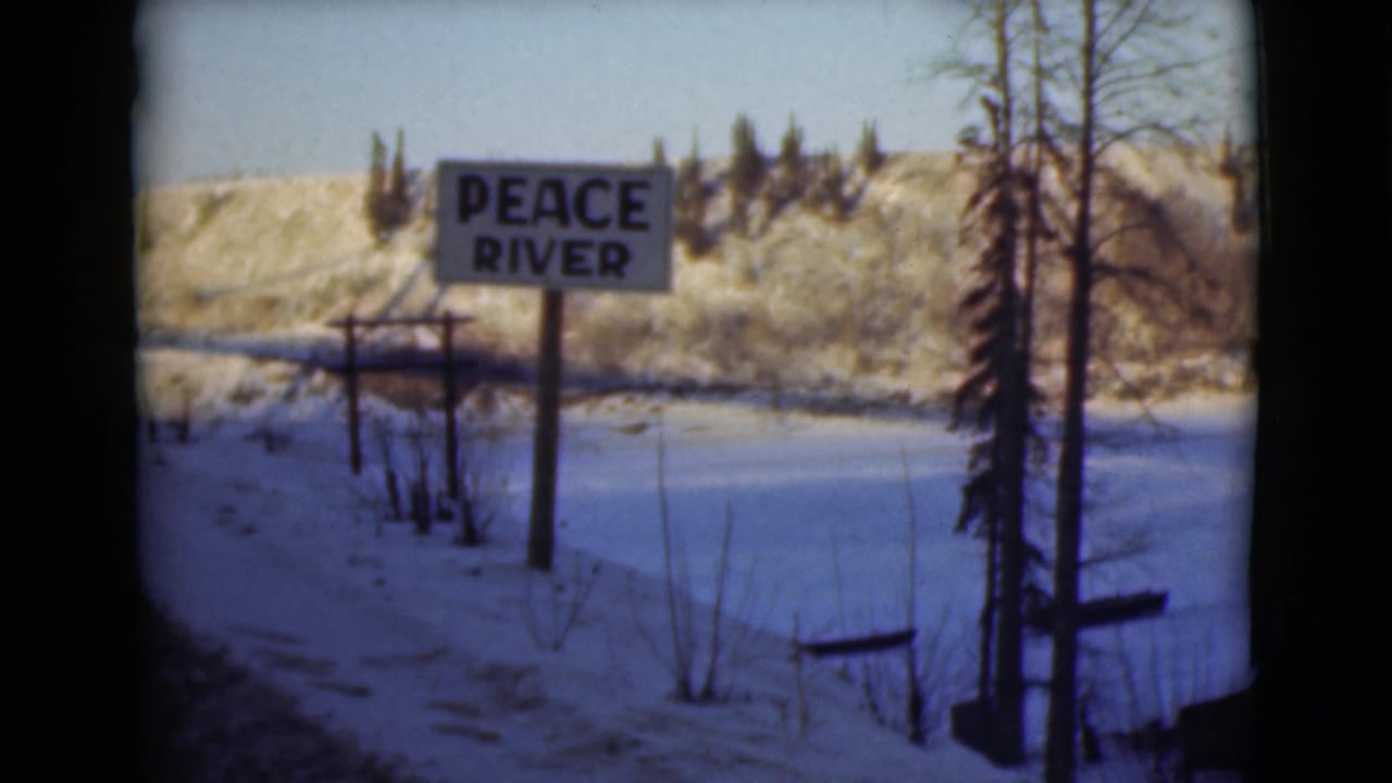 Peace River sign beside a snowy road and frozen riverside landscape.