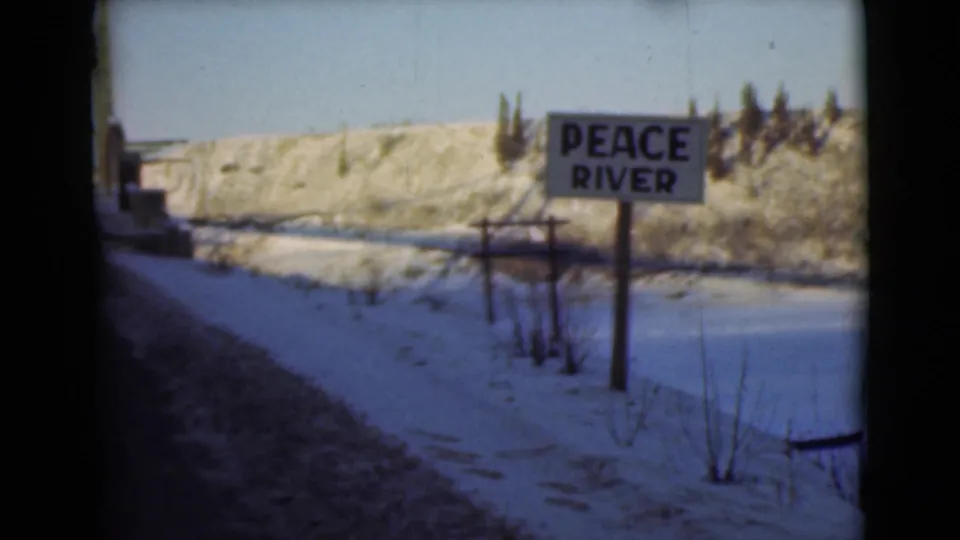 A closer moving-vehicle view of the Peace River sign shows snow, roadside tracks, sparse brush, and a pale hillside in Alaska metadata context.
