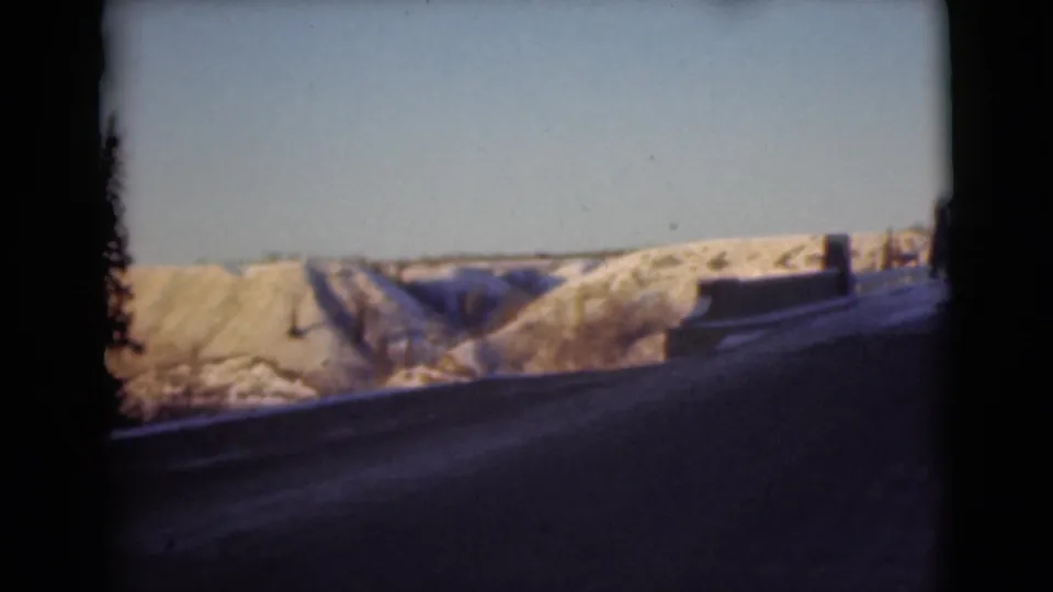 1946 Alaska 8mm frame showing the bridge roadway in shadow with snow-covered terrain and a pale sky beyond.
