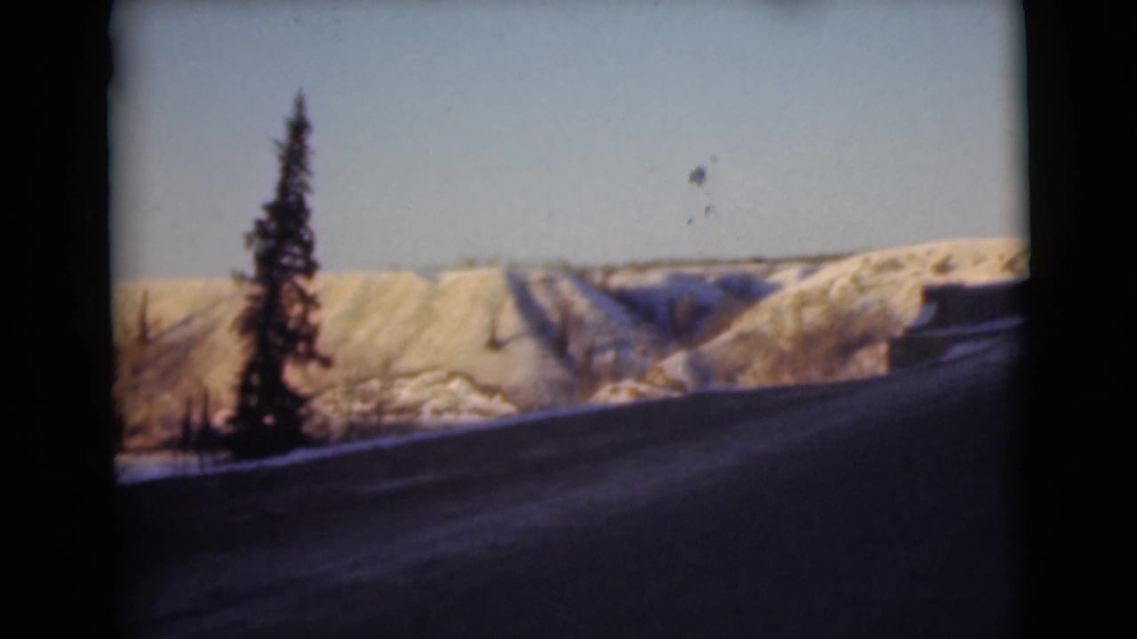 Snowy hillside and evergreen beside a dark road under a pale blue sky.