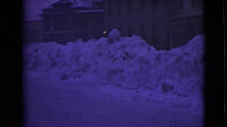 1946 Alaska 8mm frame with a purple-tinted night view of a large snowdrift after a heavy storm, with dark structures behind it.
