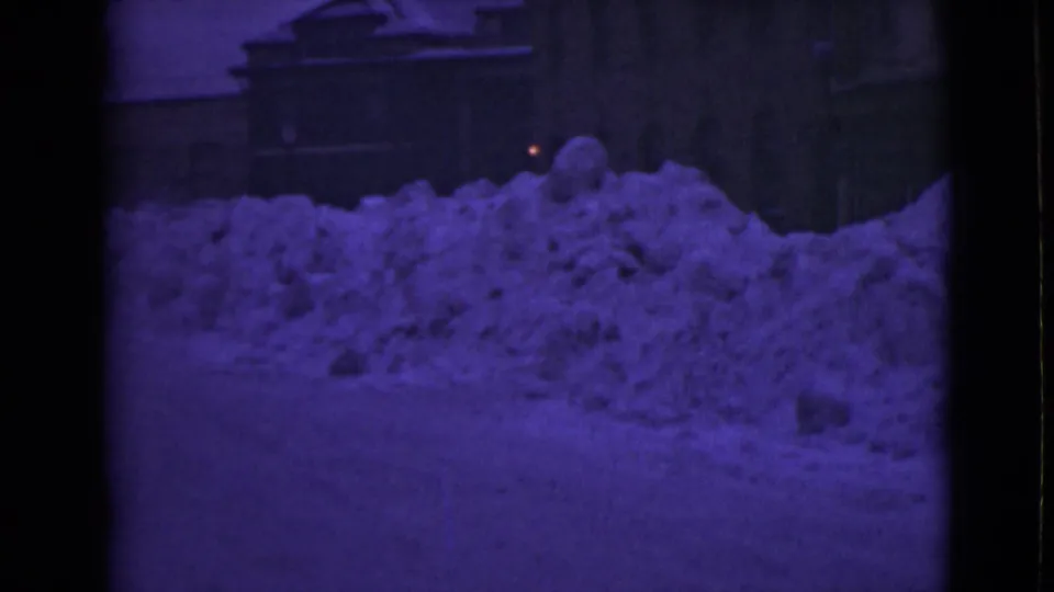 1946 Alaska 8mm view of massive snowbanks lining a road in front of shadowed buildings.