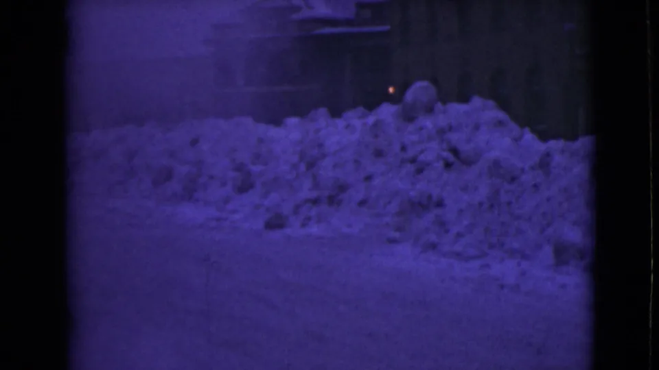 1946 Alaska home-movie frame showing tall roadside snowbanks in front of buildings during winter.