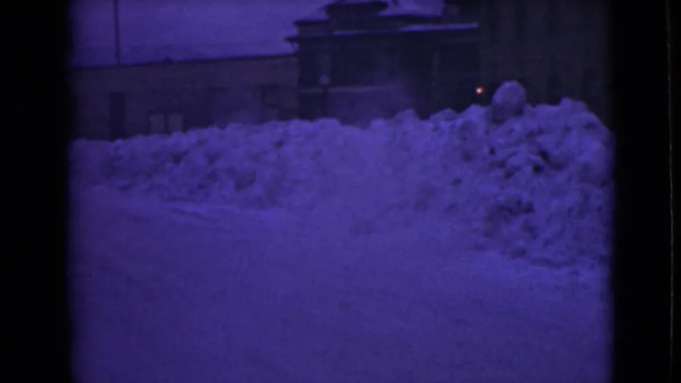 Purple-shifted 8mm frame of a snowbound Alaska street with deep drifts against nearby buildings.