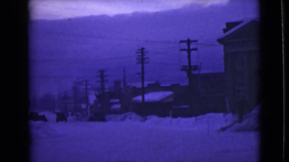 1946 Alaska home-movie view of a snow-covered street with pole lines, distant buildings, low hills or mountains, and heavy accumulated snow.