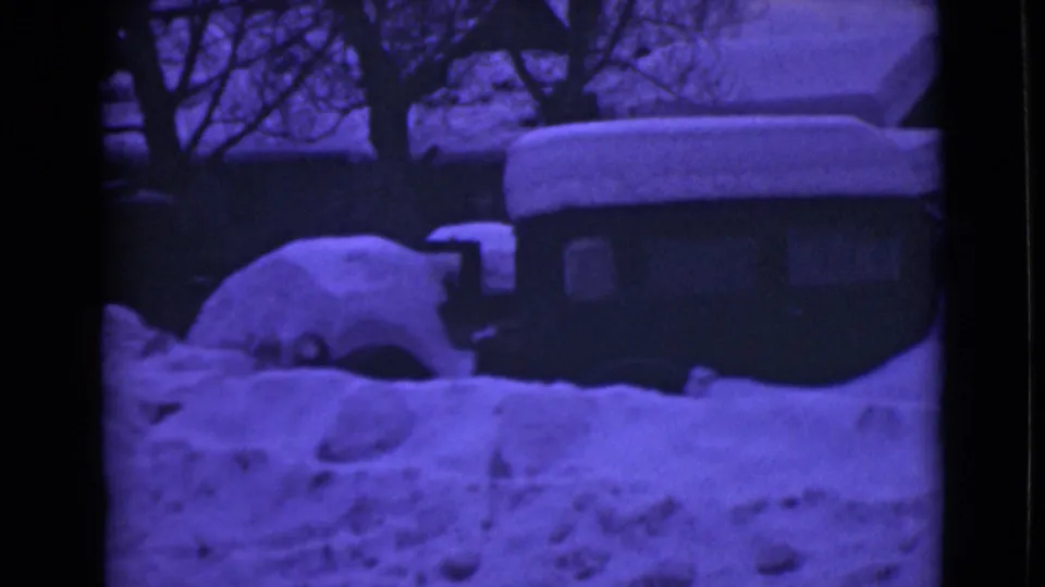 1946 Alaska home-movie view of a rounded car mostly buried in snow beside a dark building and winter trees.