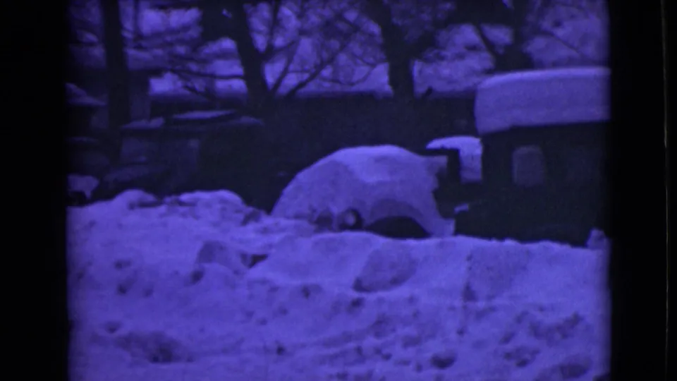 1946 Alaska 8mm frame showing cars or trucks nearly covered by snow beside a dark snowy road at night.