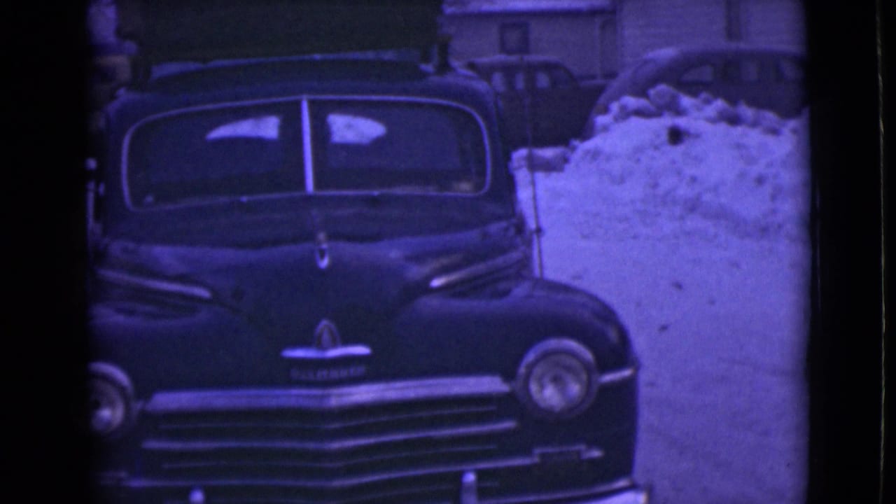1946 Alaska 8mm frame showing a vintage American car parked amid deep snowbanks in a winter setting.