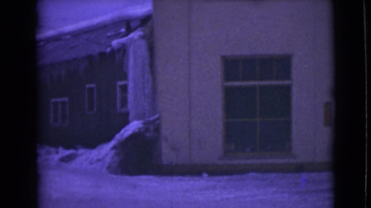 1946 Alaska 8mm frame showing a snow-covered building facade with a large window, icicles along the roofline, and a purple film tint.