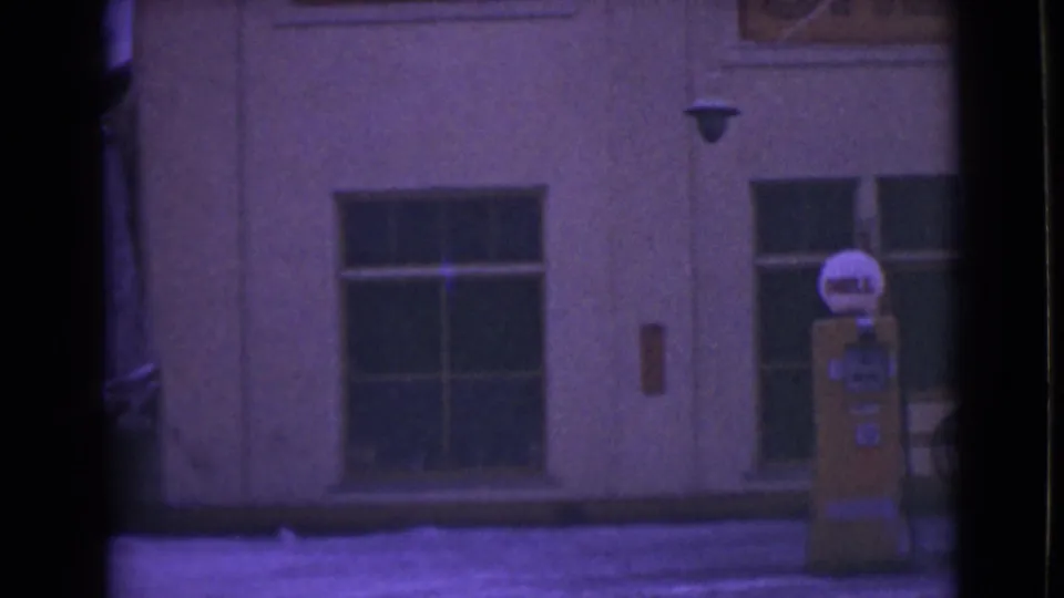 1946 Alaska 8mm frame showing a yellow Shell gas pump near snow-covered ground and large building windows.