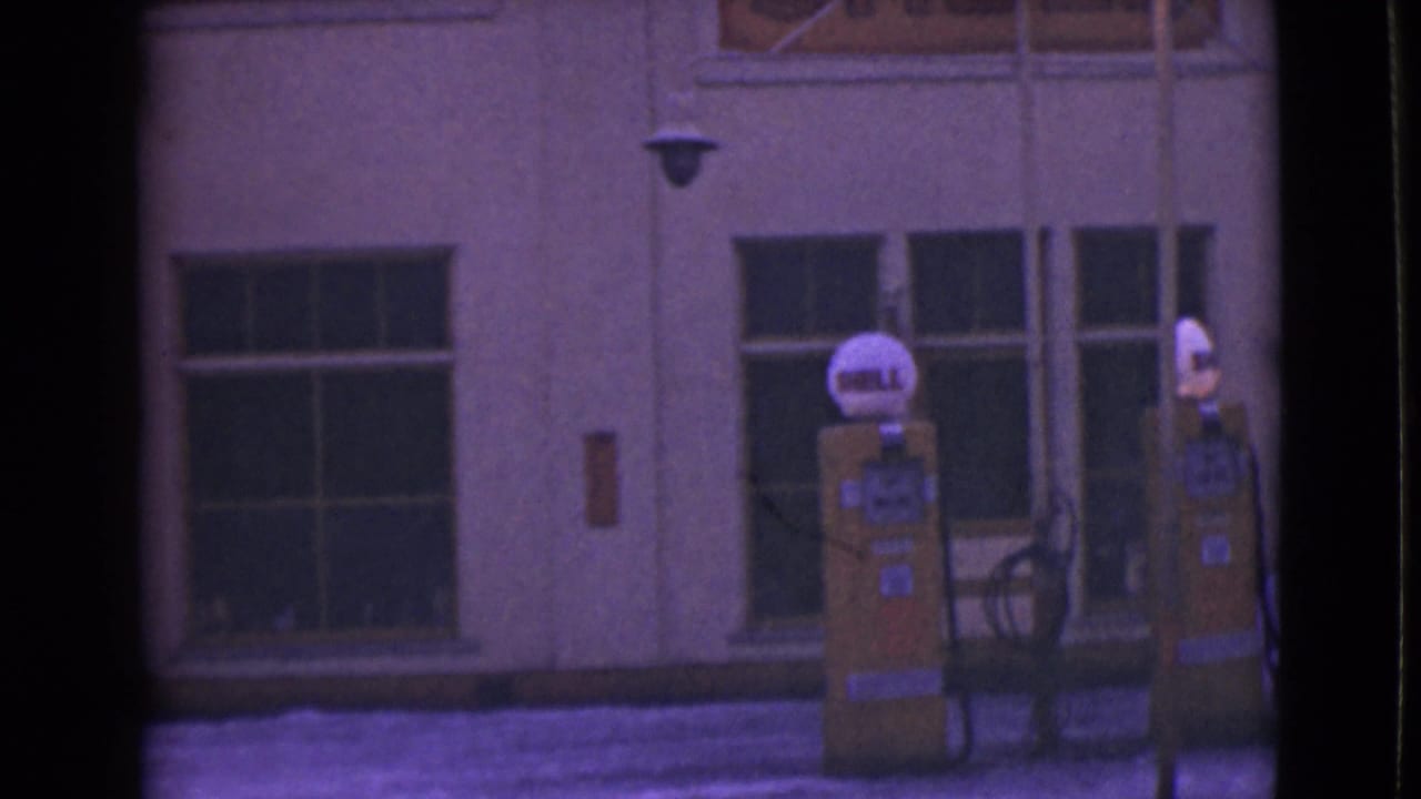 Two yellow Shell gas pumps outside a cream building with snow along the curb.
