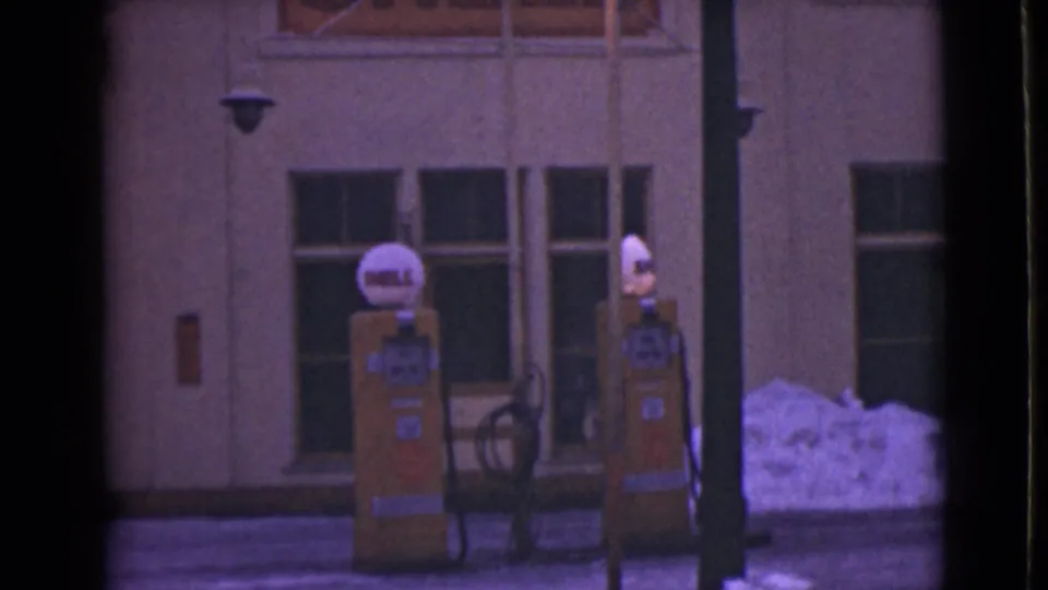 1946 Alaska service-station frame with yellow Shell pumps centered against a plain facade and snow bank near the curb.