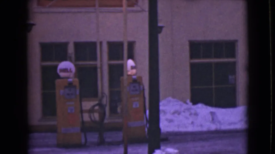 Final 8mm frame of the 1946 Alaska gas station exterior, showing Shell pumps, dark windows, a vertical doorway edge, and piled snow.