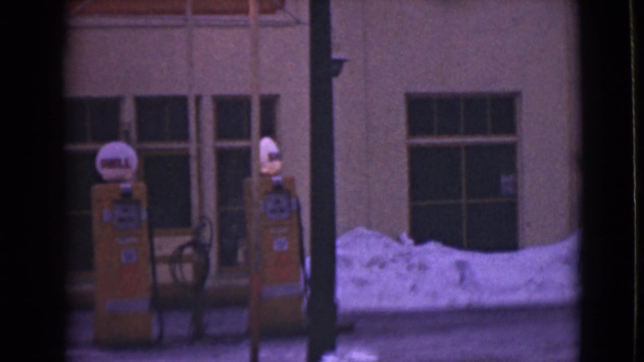 Two yellow Shell gas pumps stand beside a snowy storefront with large windows.