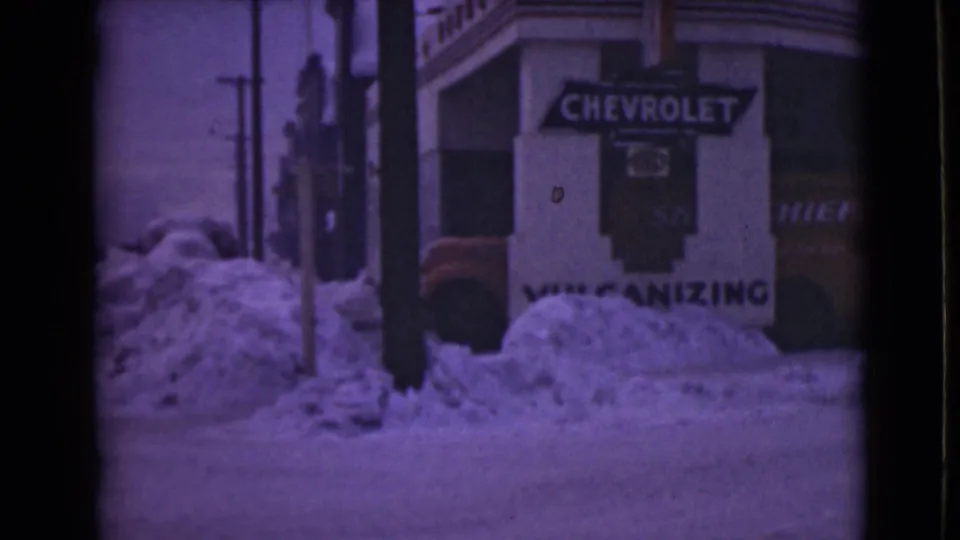 Snowy 1946 Alaska street view with a Chevrolet sign, vulcanizing text, and piled snow along the curb.