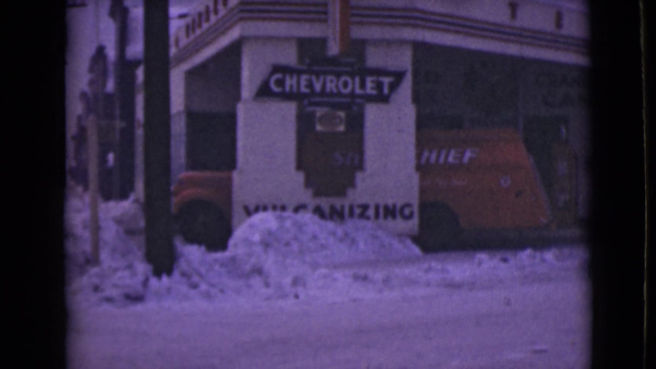Red Chevrolet Chief van parked beside snowbanks outside a commercial building with Chevrolet signage.