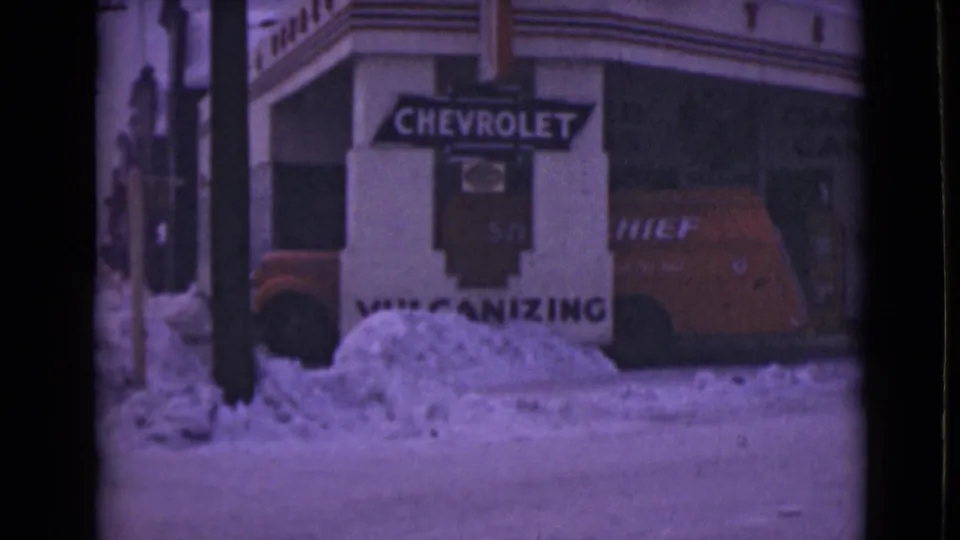 1946 Alaska home-movie frame showing a red Chevrolet Chief van near a snowy storefront with Chevrolet and vulcanizing signs.
