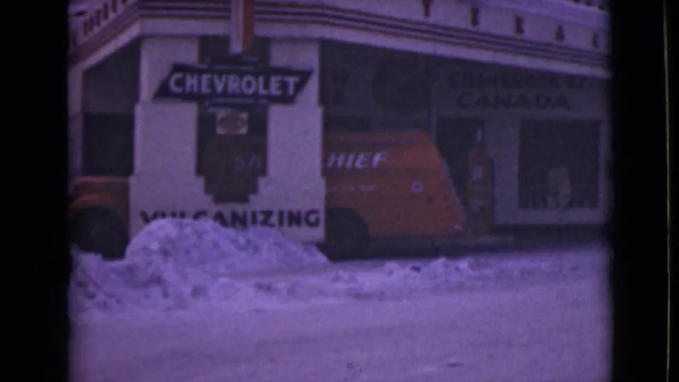1946 Alaska frame showing a red van by a Chevrolet sign, vulcanizing lettering, snowbanks, and faint storefront text.