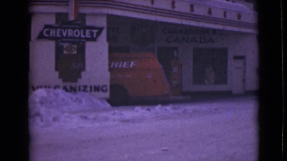 1946 Alaska home-movie view of a red Chief van, Chevrolet signage, snowbanks, and commercial windows on a winter street.