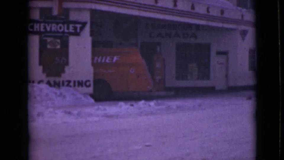 1940s 8mm frame of a red Chief van near a snowy storefront with Chevrolet and Canada lettering visible.