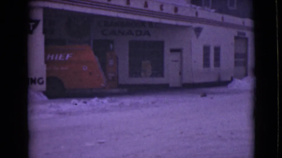 1940s home-movie frame showing the red Chief van, white facade, windows, and snow piled along the building.