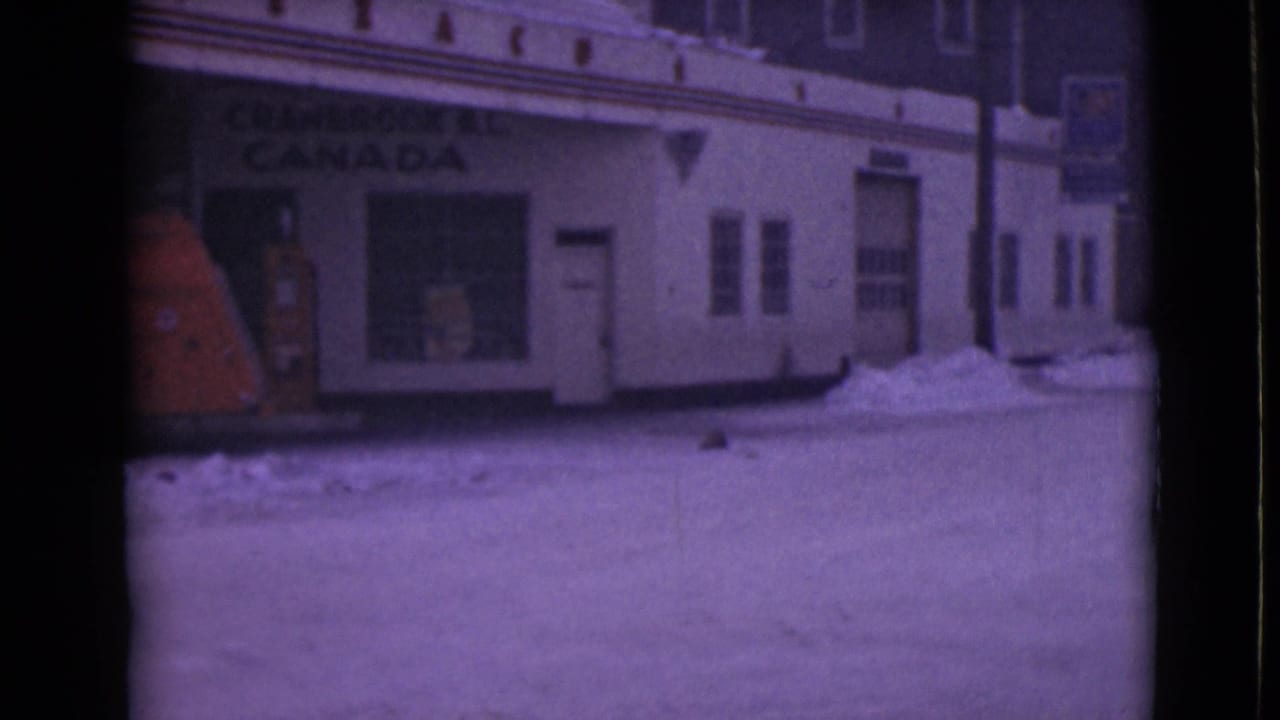 1940s 8mm frame showing a snowy roadside storefront with Cranbrook B.C. Canada signage and an orange fuel pump.