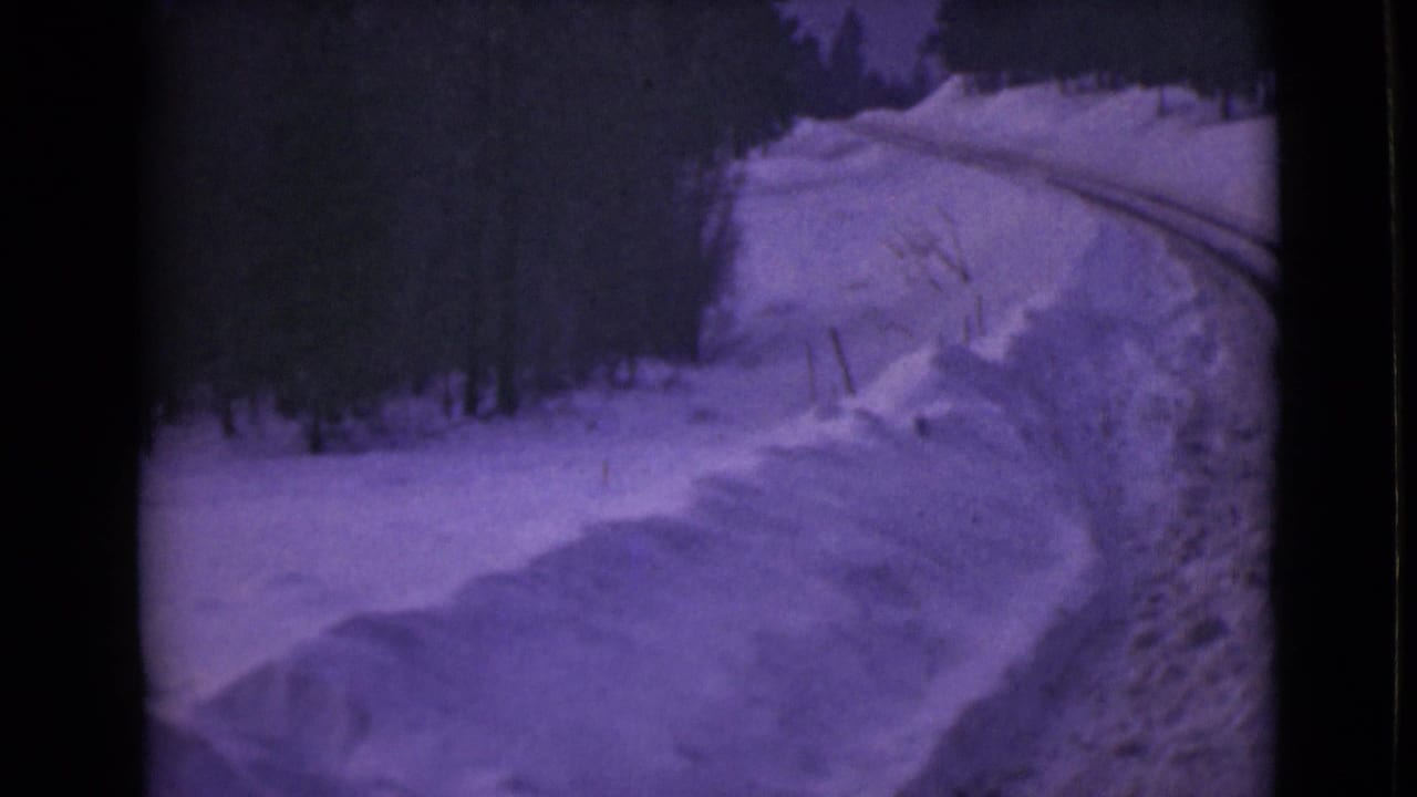1946 Alaska frame with a snow-covered roadside, high plowed-looking banks, and dark forest beyond the curve.