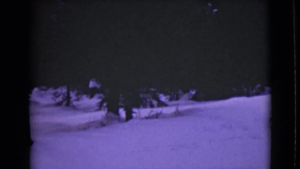 1946 Alaska home-movie frame with snow-covered terrain, a dark evergreen line, and faint surface marks in the snow.