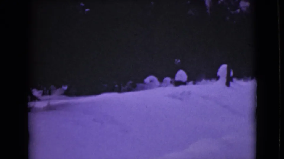 1946 Alaska frame showing deep snow, faint footprints or tracks, dark evergreen silhouettes, and purple-tinted 8mm texture.