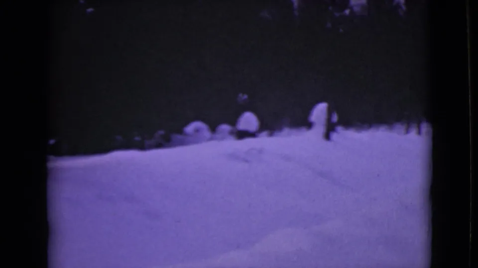 1946 Alaska 8mm frame showing a snow-covered forest road or track bordered by dark pines and rounded snow mounds.