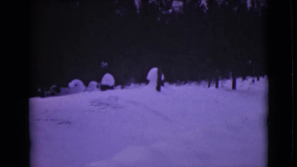 1946 Alaska 8mm frame of a snow-covered road through pines, with a small distant upright person or figure near the roadside.