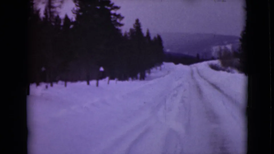 1946 Alaska home-movie view of a snow-covered road bordered by forest, with a distant hillside beyond.