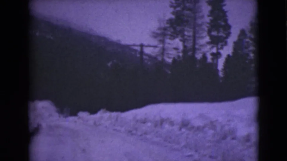 1946 Alaska 8mm frame showing a snow-lined road, evergreen trees, and a utility pole near a dark mountain slope.