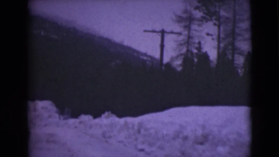 1946 Alaska 8mm frame showing roadside snowbanks, a utility pole, tall trees, and a dark mountain backdrop.