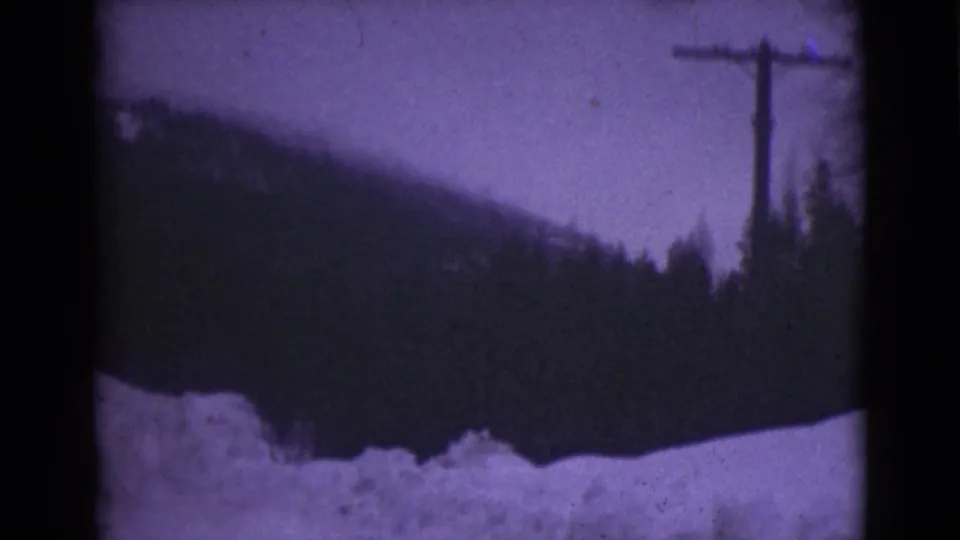1946 Alaska 8mm frame showing a snowbank in the foreground and a forested mountain slope beneath a pale winter sky.
