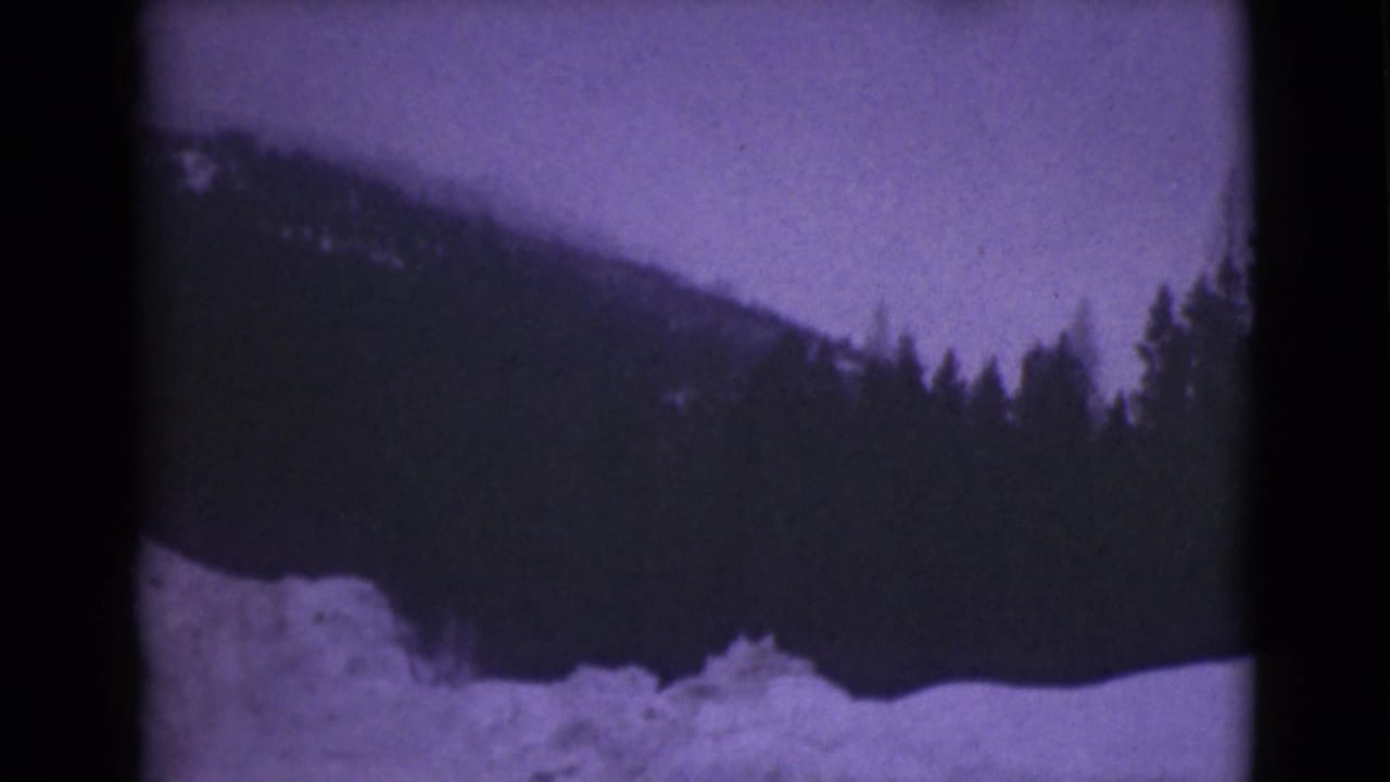 1946 Alaska 8mm frame showing a snowy foreground, dark evergreen hillside, and pale winter sky with soft focus and purple film cast.