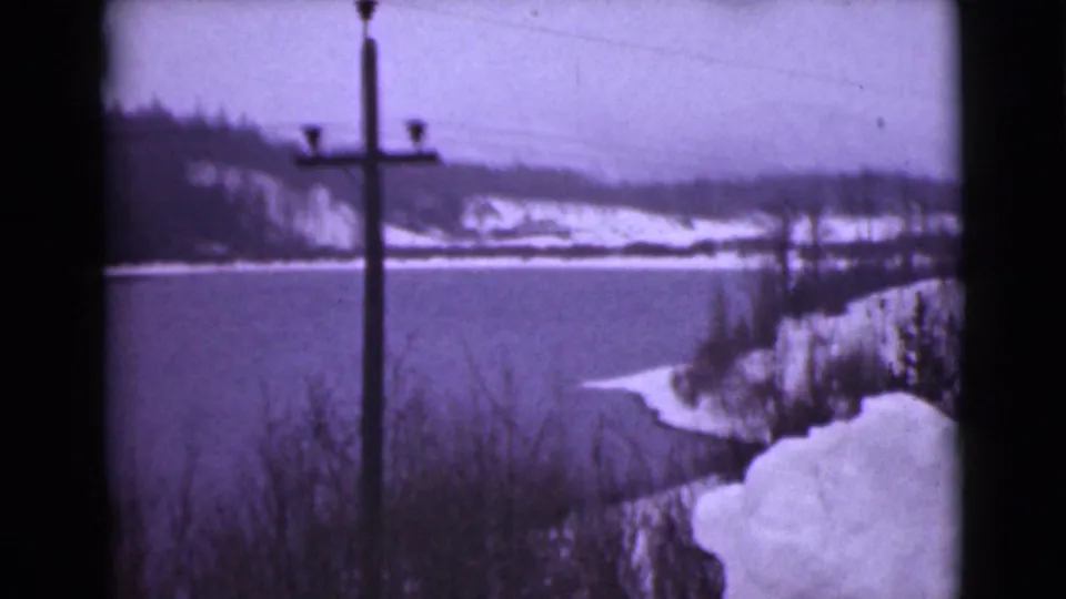 1946 Alaska 8mm frame looking across a snow-edged lake toward wooded hills, with a utility pole centered in the foreground.