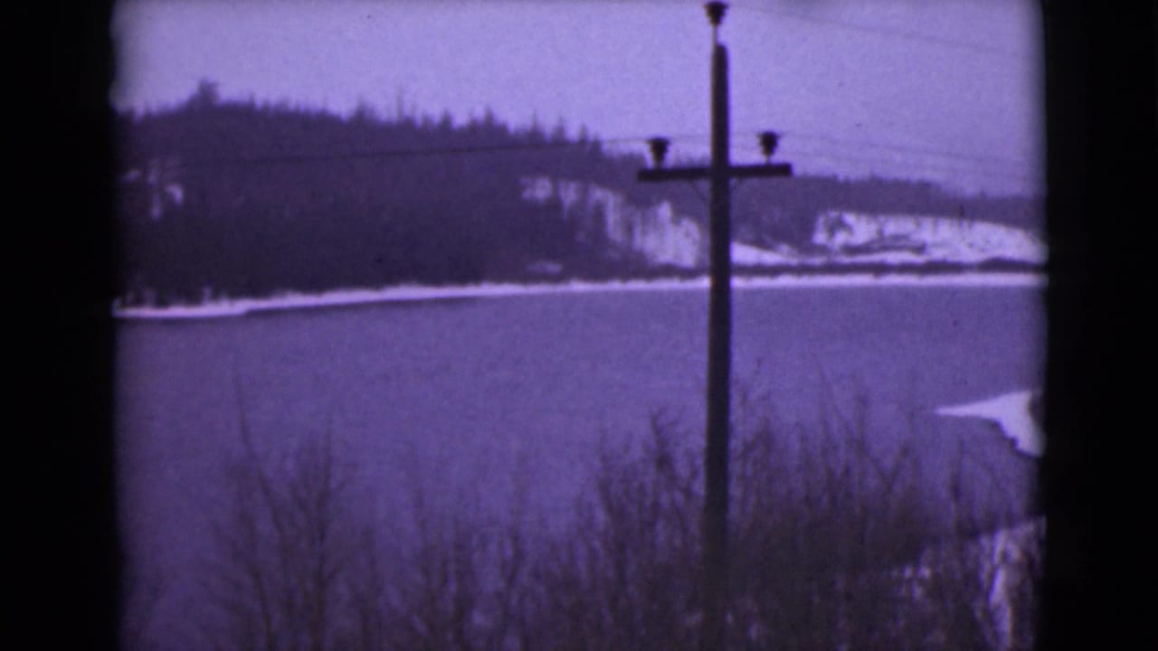 1946 Alaska 8mm frame showing a winter lake, dark wooded hills, overhead wires, and a telephone pole in the foreground.
