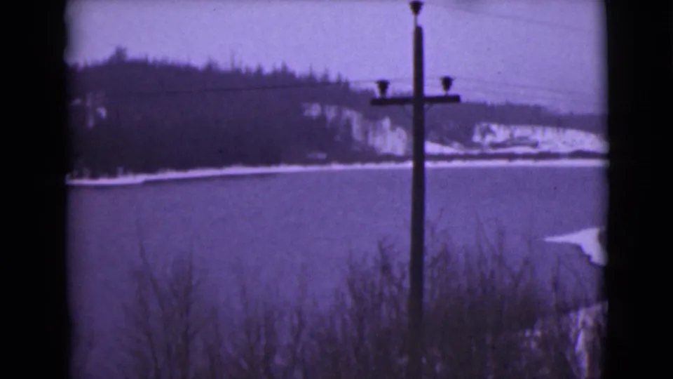 1946 Alaska 8mm frame showing a winter lake, dark wooded hills, overhead wires, and a telephone pole in the foreground.