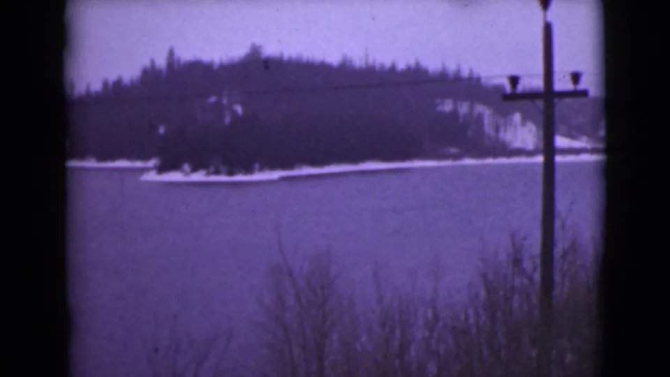 1946 Alaska 8mm frame showing a snowy shoreline, dark trees, calm lake water, and a telephone pole partly near the right edge.