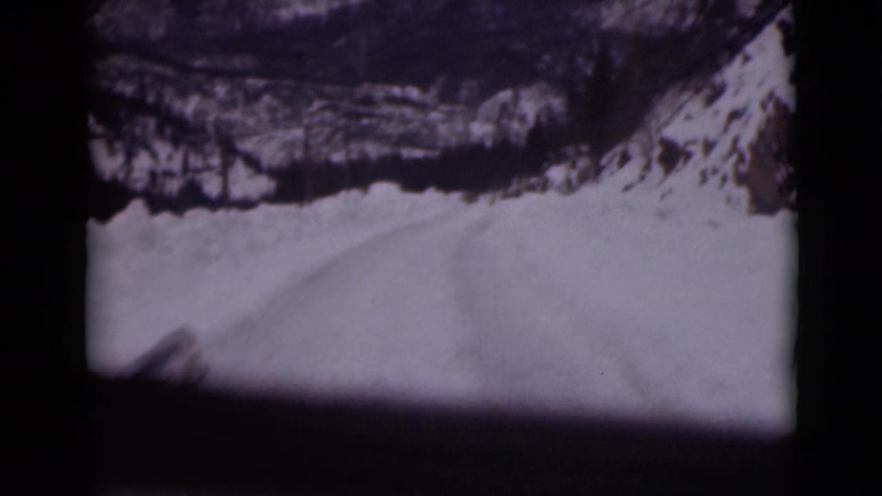 Snow-covered mountain road seen through dark vehicle-window framing.