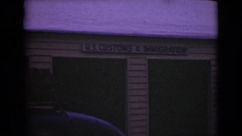 Frame showing a garage-like U.S. Customs & Immigration building in the supplied Alaska 1946 travel clip, with dark doors and film color shift.