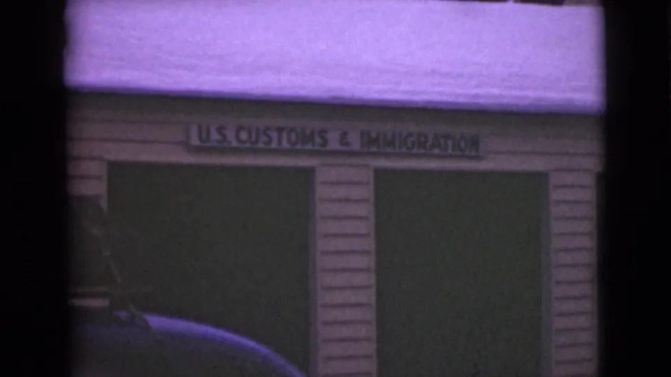 1946 Alaska 8mm frame showing a snow-covered U.S. Customs and Immigration wood building facade with a partial car at left.