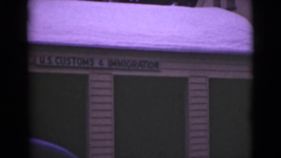 1946 Alaska 8mm frame centered on the U.S. Customs and Immigration sign above a snow-laden wood facade.