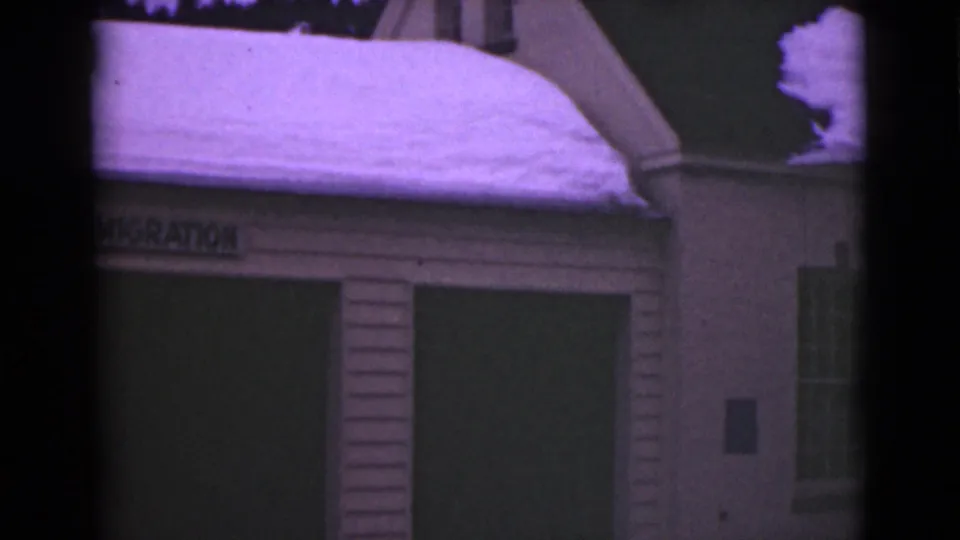1946 Alaska 8mm frame showing the customs building under snow with part of a neighboring wall and window visible at right.