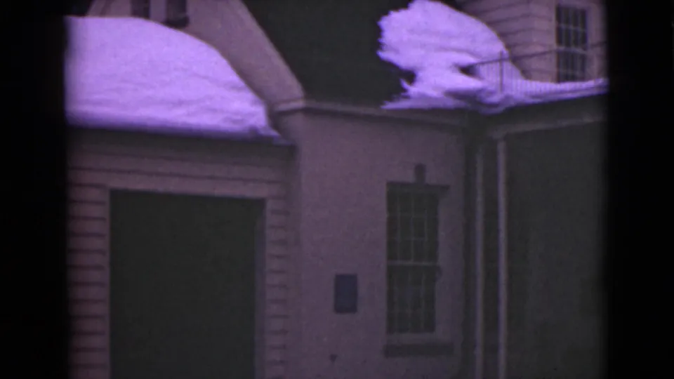 1946 Alaska 8mm frame with the pan revealing a building corner, dark wall panel, tall window, railing, and thick snow on the roof edge.